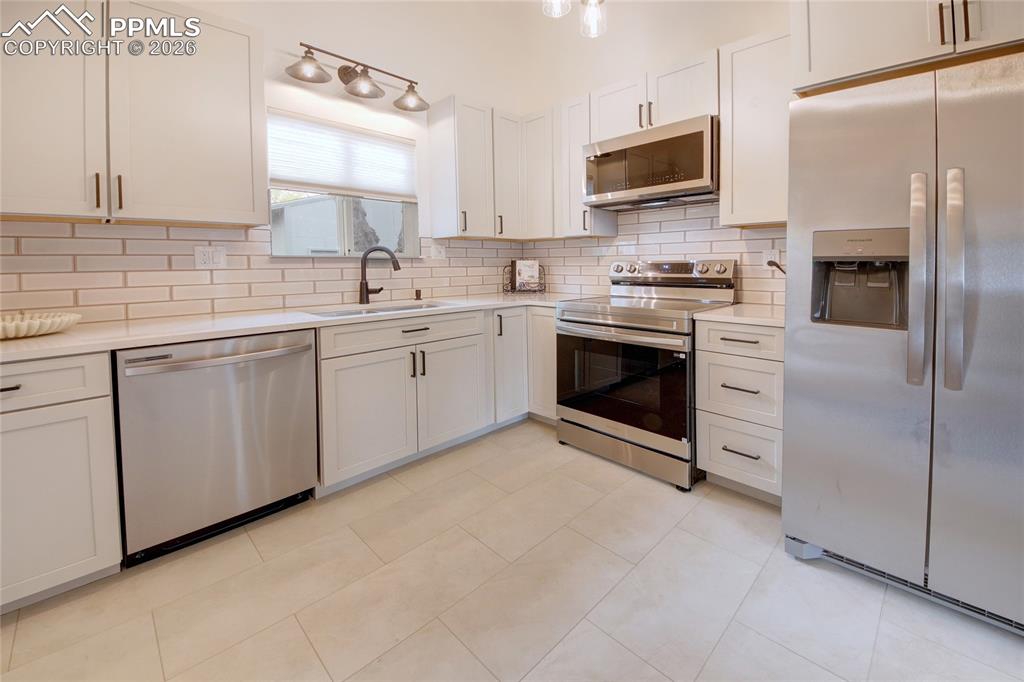 Image 7 of 27: Contemporary kitchen featuring white cabinetry, subway tile backsplash, sta