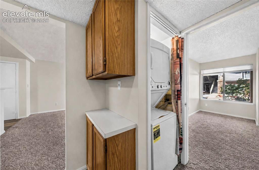 Image 15 of 22: Built-in wood-finish cabinetry, white countertop, and stacked laundry appli
