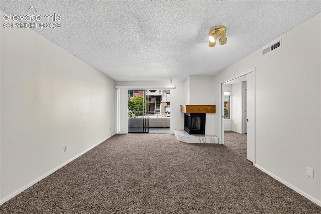 Image 7 of 22: Spacious living area featuring a corner fireplace with a wood mantel, slidi