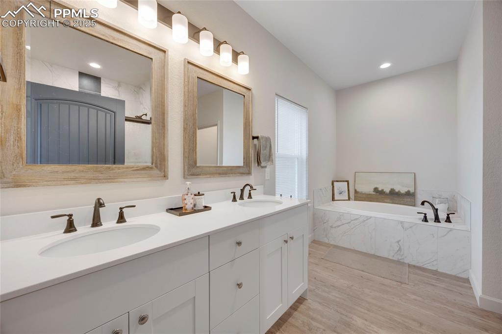 Image 21 of 37: Full bath with a garden tub, light wood-style flooring, double vanity, and