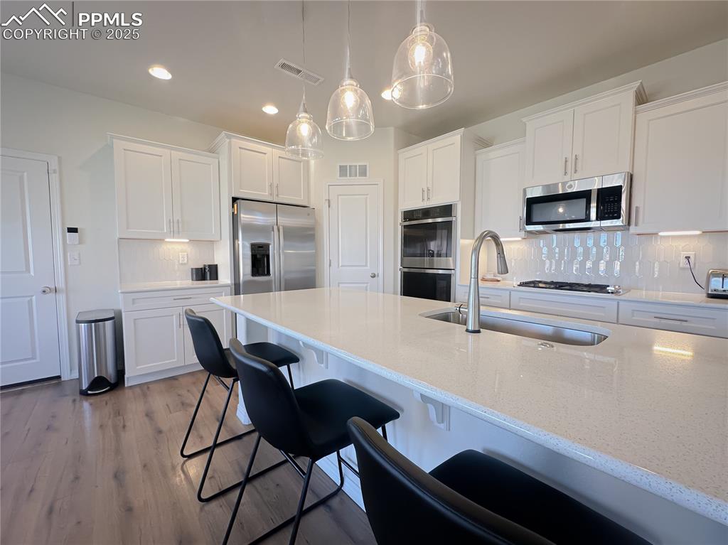 Image 18 of 42: Kitchen with backsplash, white cabinets, pendant lighting, appliances with