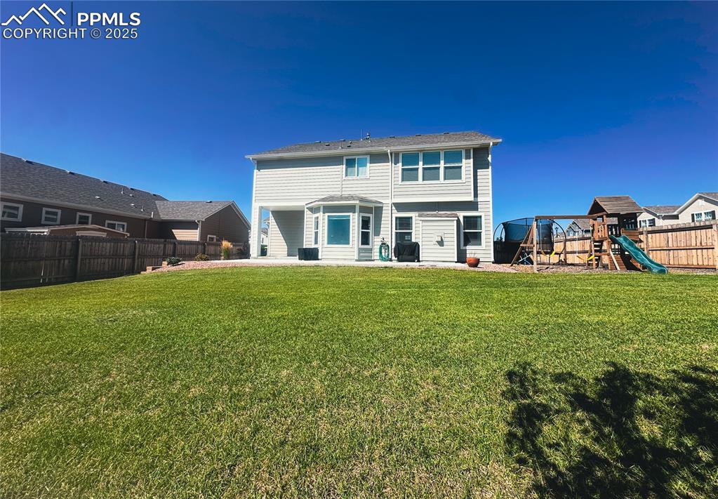 Image 38 of 42: Rear view of house with a fenced backyard, a playground, and a patio area