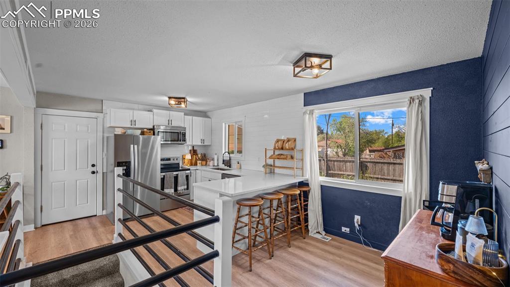 Image 14 of 42: Open-concept kitchen featuring white cabinetry, stainless steel appliances,