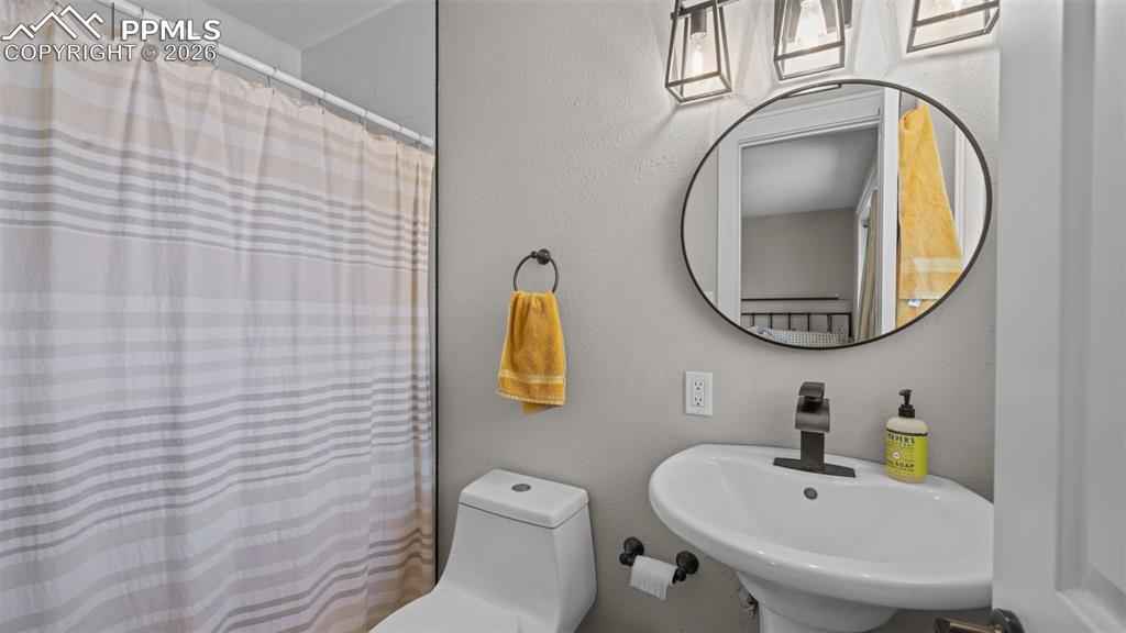 Image 18 of 42: Pedestal sink with matte black faucet, framed round mirror, and three-light