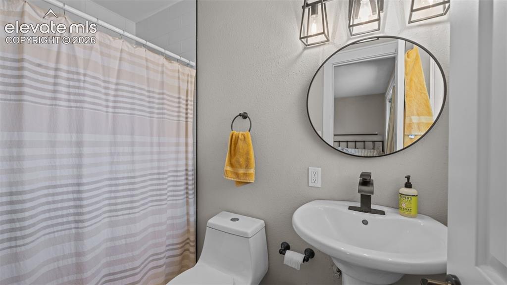 Image 19 of 43: Pedestal sink with matte black faucet, framed round mirror, and three-light