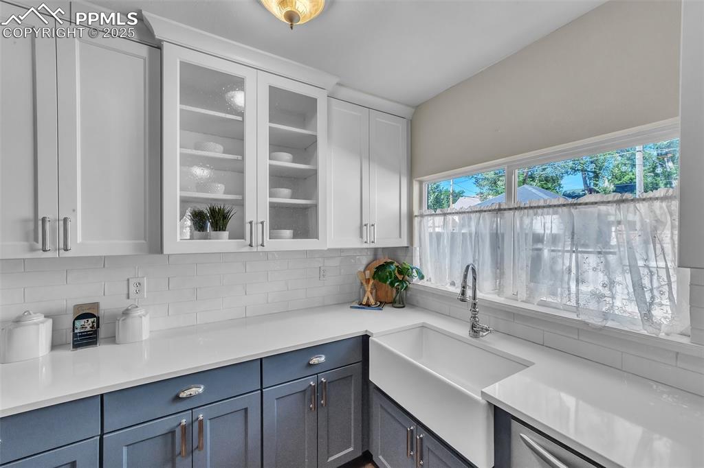 Image 12 of 49: Kitchen featuring backsplash, white cabinets, glass insert cabinets, and qu