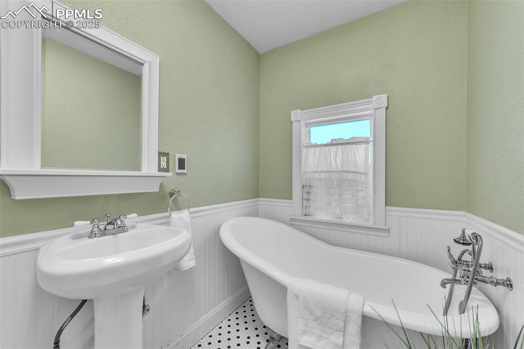Image 15 of 49: Bathroom with a wainscoted wall and original steel freestanding tub, with h