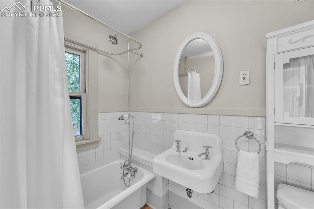 Image 19 of 49: Bathroom with tile walls and wainscoting with original steel tub and featur