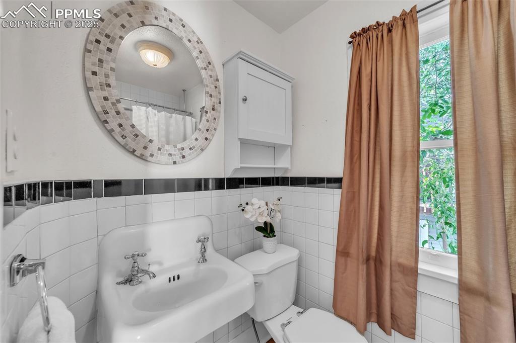 Image 28 of 49: Bathroom featuring tile walls and a wainscoted wall, with original steel tu