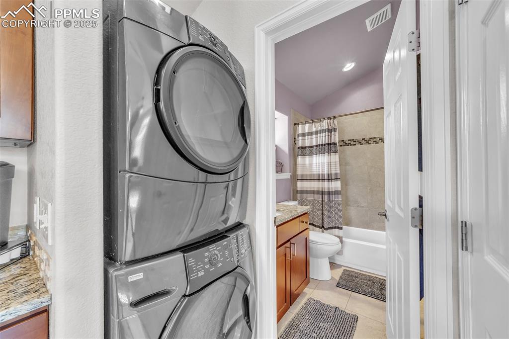 Image 34 of 49: Apartment: Full bathroom with stacked washer and clothes dryer, vanity, til