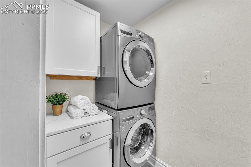 Image 8 of 49: Laundry area featuring stacked washer / dryer and cabinet space