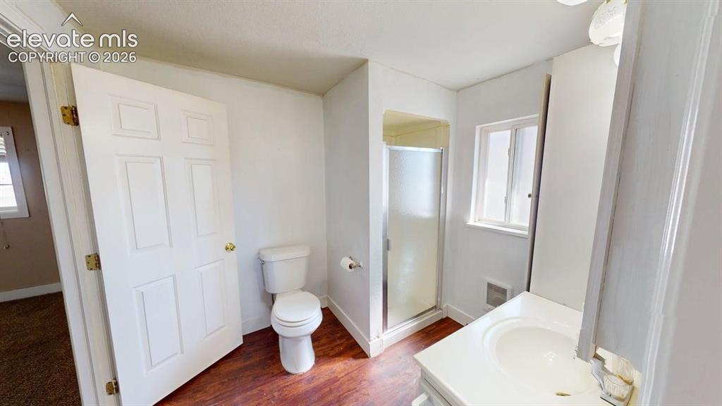 Image 17 of 23: White paneled door, wood-finish flooring, white toilet, glass-enclosed show