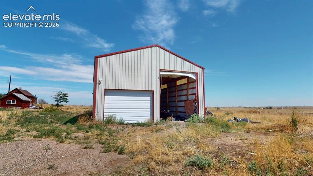 Image 4 of 23: Metal-clad storage building with a rolled garage door, open bay, and pitche