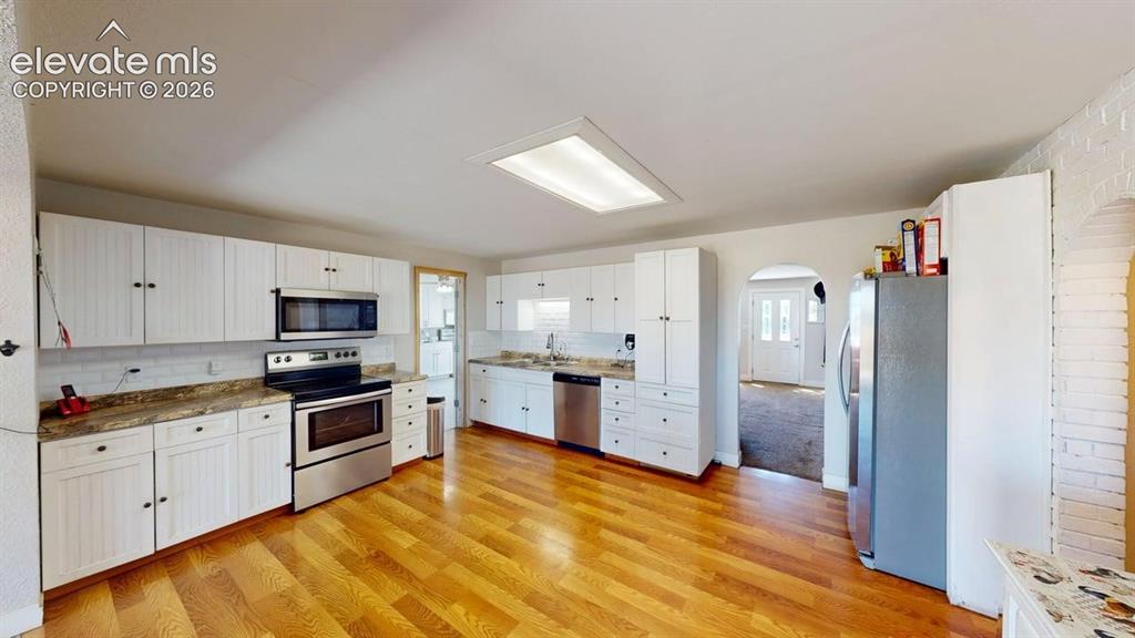 Image 5 of 23: Kitchen featuring wood-finish flooring, white cabinetry, stainless steel ap
