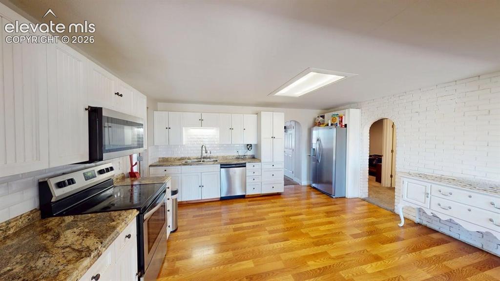 Image 6 of 23: White cabinetry, wood-finish flooring, stainless steel appliances, speckled