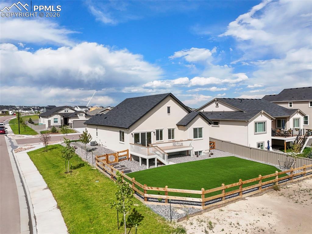 Image 33 of 37: Rear exterior featuring a spacious artificial turf lawn, an elevated wood d