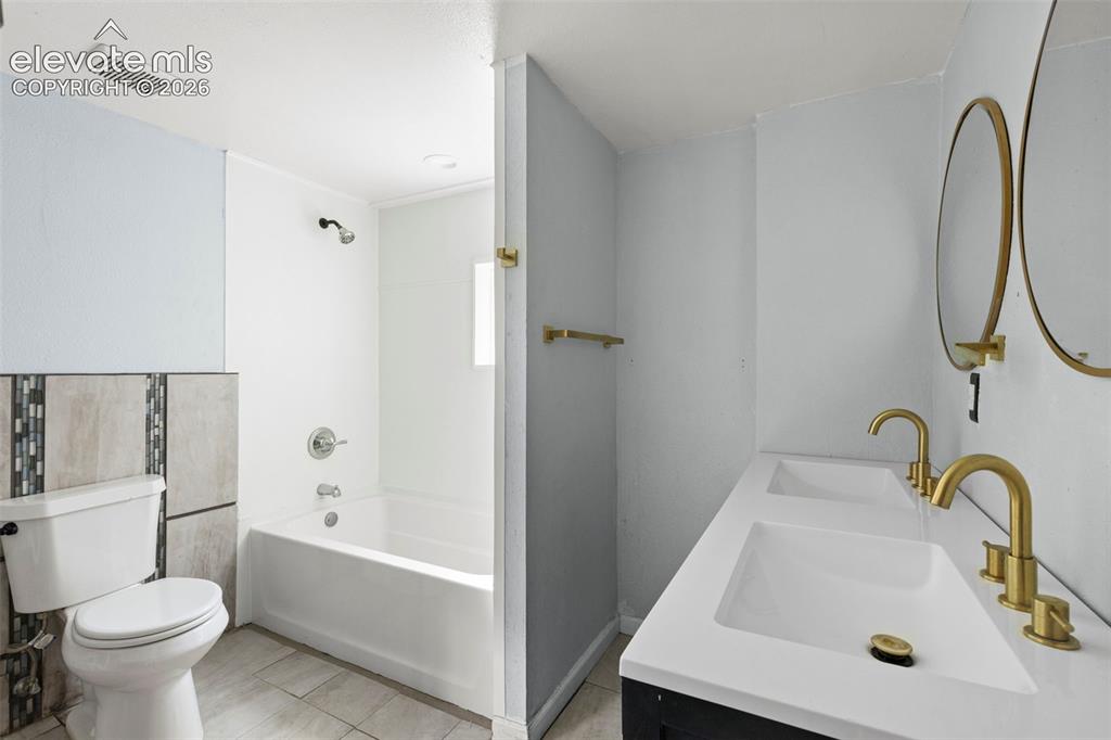 Image 23 of 24: Full bathroom featuring a white bathtub with a shower head, toilet, and a d