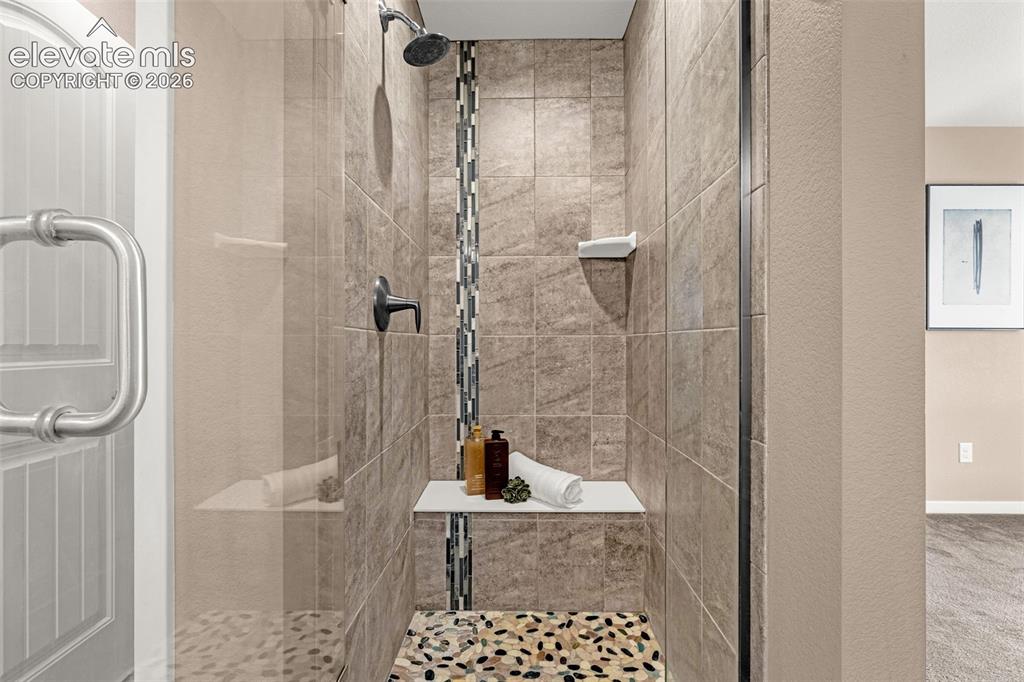 Image 20 of 28: Glass-enclosed shower featuring large format wall tile, a decorative vertic
