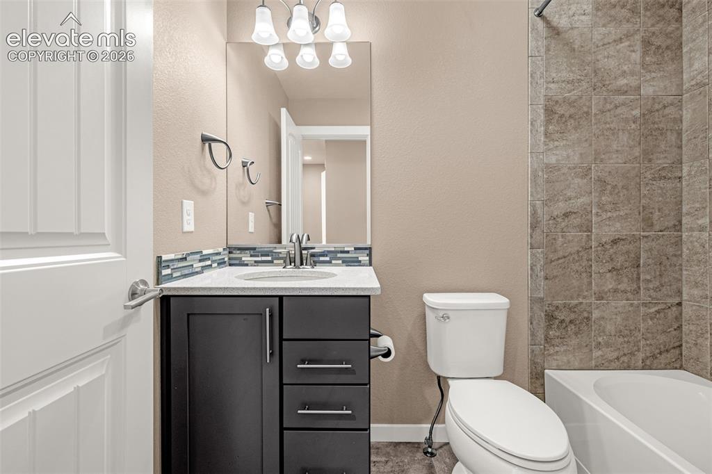 Image 21 of 28: Vanity with light-toned countertop, glass tile backsplash, and dark cabinet