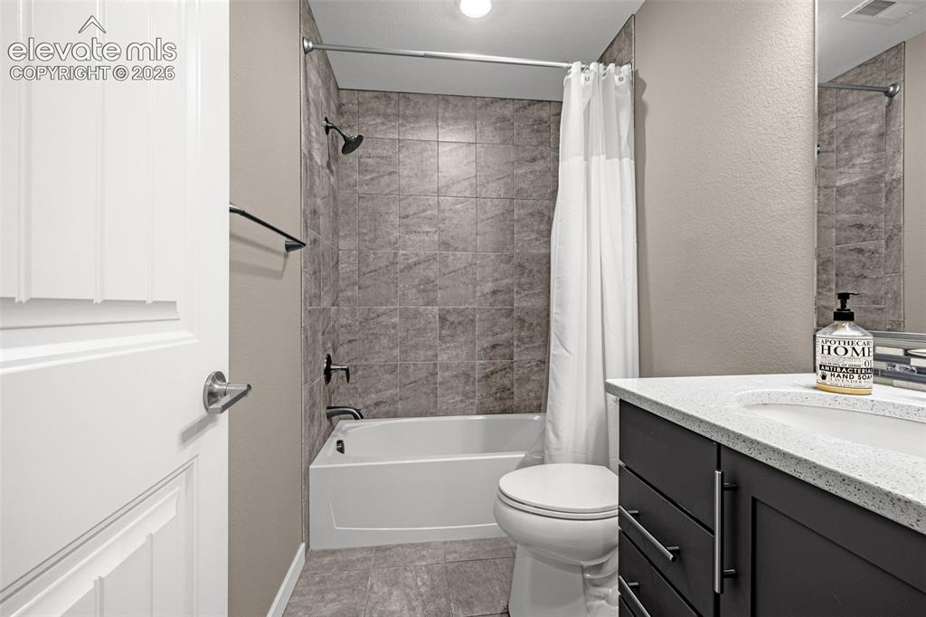 Image 23 of 28: Tub-shower combination with tiled surround, dark wood-finish vanity, and in
