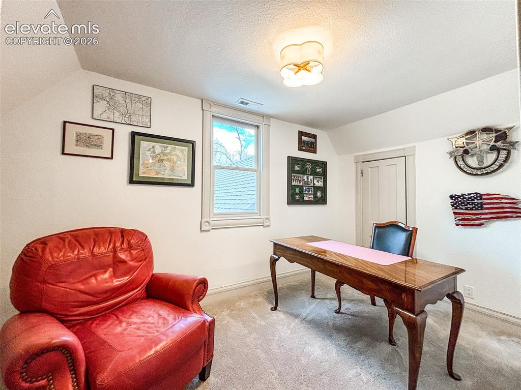 Image 26 of 33: Carpeted room featuring sloped ceilings, a window with decorative trim, and