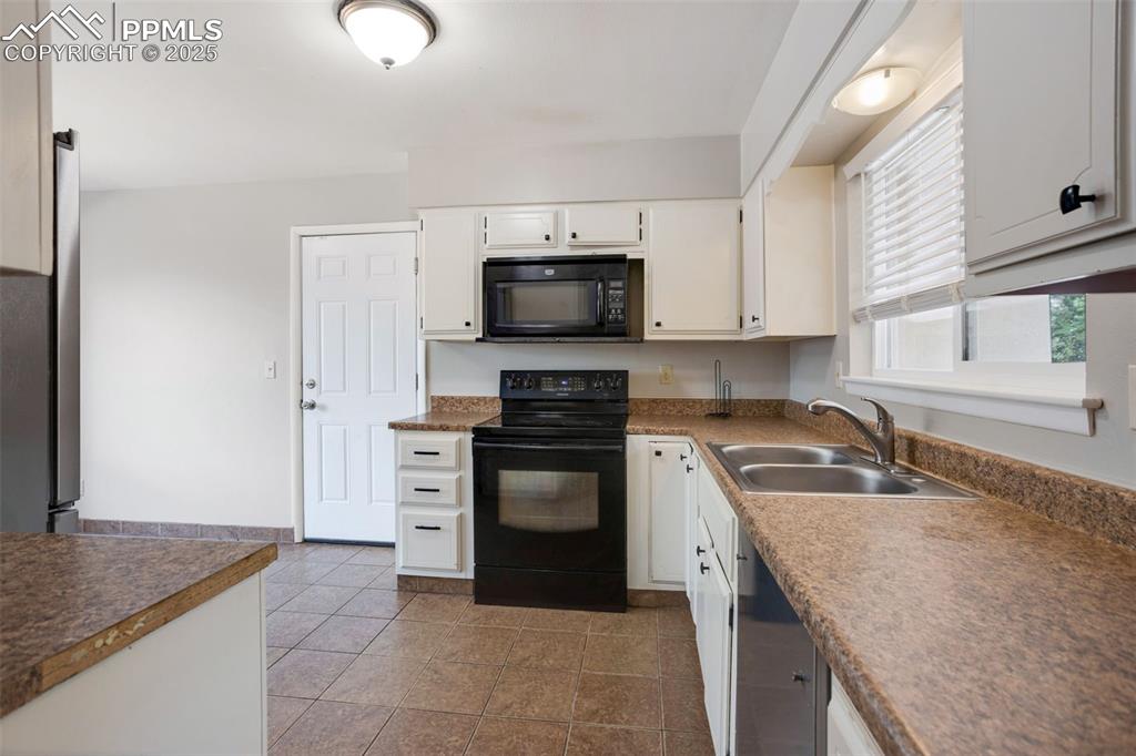 Image 9 of 35: Kitchen featuring black appliances, white cabinetry, dark tile patterned fl