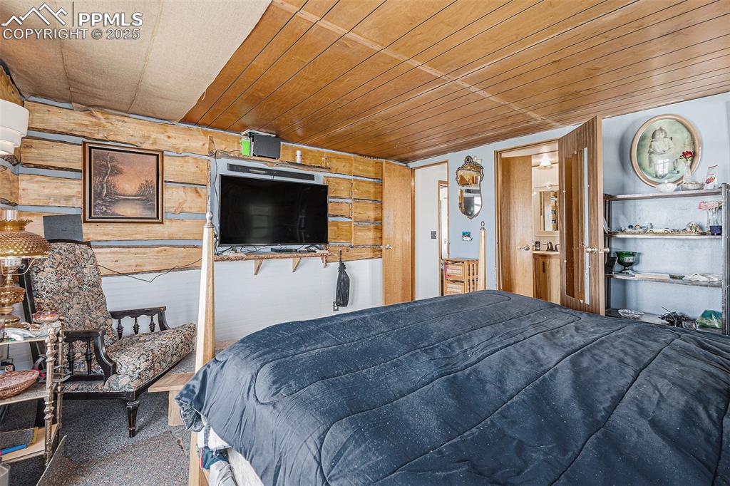 Image 11 of 25: Bedroom with carpet floors, wooden walls, and wooden ceiling