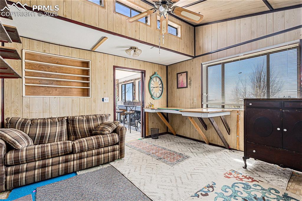 Image 13 of 25: Carpeted living area with a ceiling fan, wood walls, and a healthy amount o