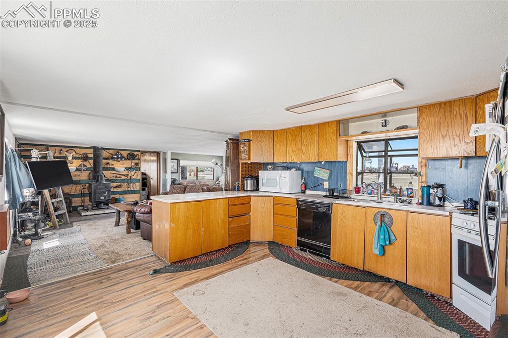 Image 6 of 25: Kitchen featuring a wood stove, a peninsula, white appliances, light counte
