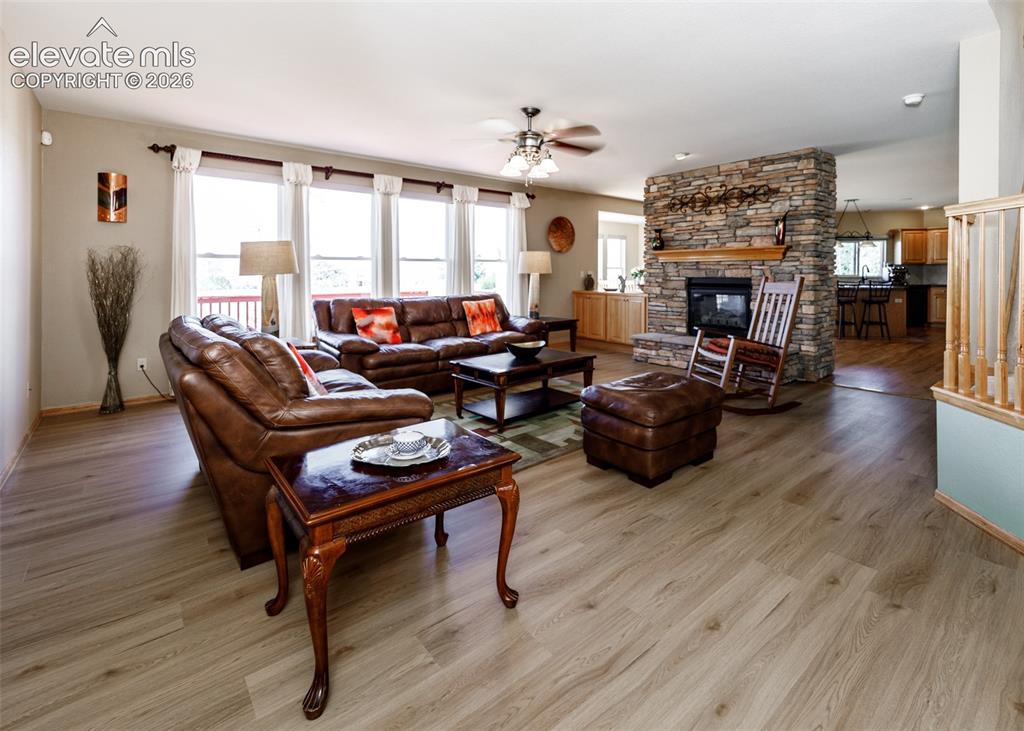 Image 22 of 48: Wood-finish flooring, stone-clad fireplace with wood mantel, ceiling fan wi