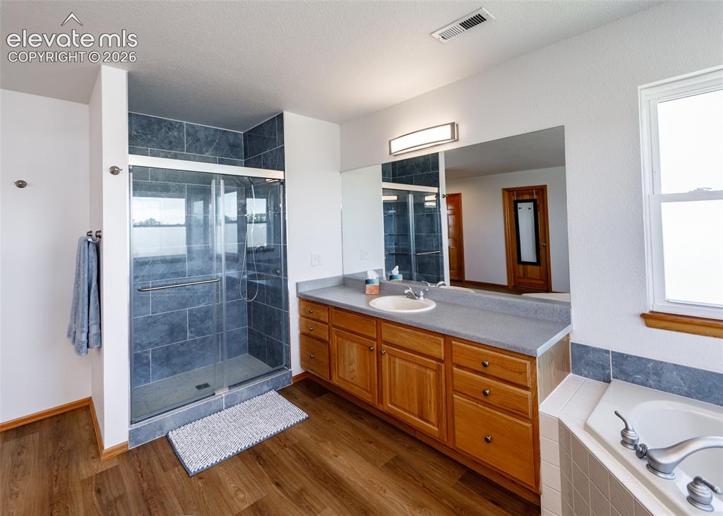 Image 27 of 48: Glass-enclosed shower with dark tile surround, single vanity with wood cabi