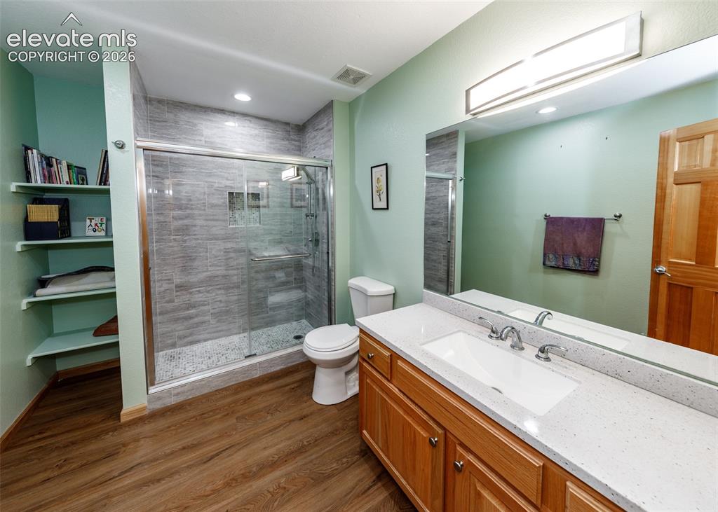 Image 32 of 48: Wood-finish flooring, built-in shelving, glass-enclosed shower with tiled w