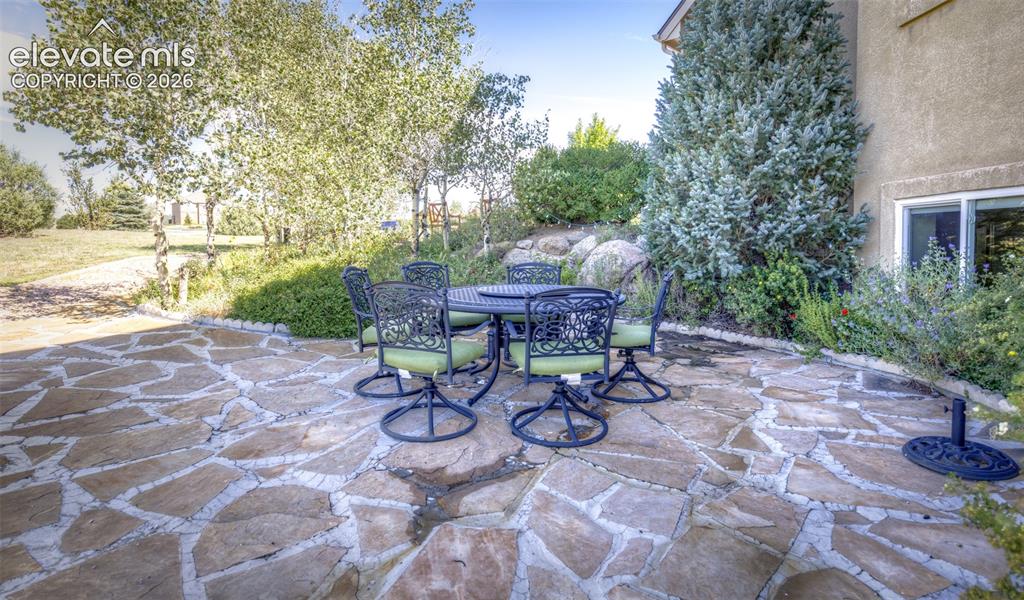 Image 48 of 48: Flagstone patio with a stucco exterior, mature evergreen, and varied foliag