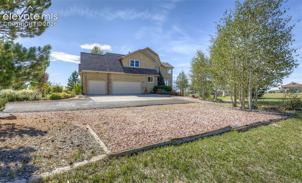 Image 5 of 48: Stucco exterior with a multi-car garage, asphalt driveway, mature trees, an