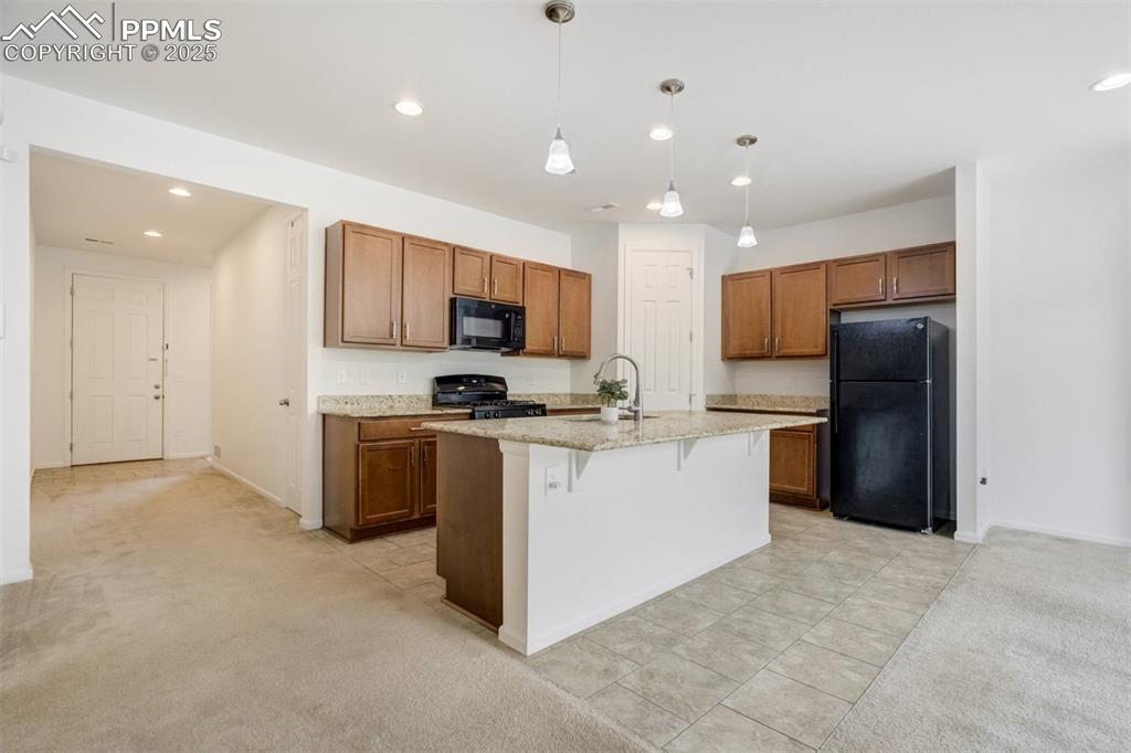 Image 5 of 36: Kitchen featuring black appliances, brown cabinets, a breakfast bar area, l