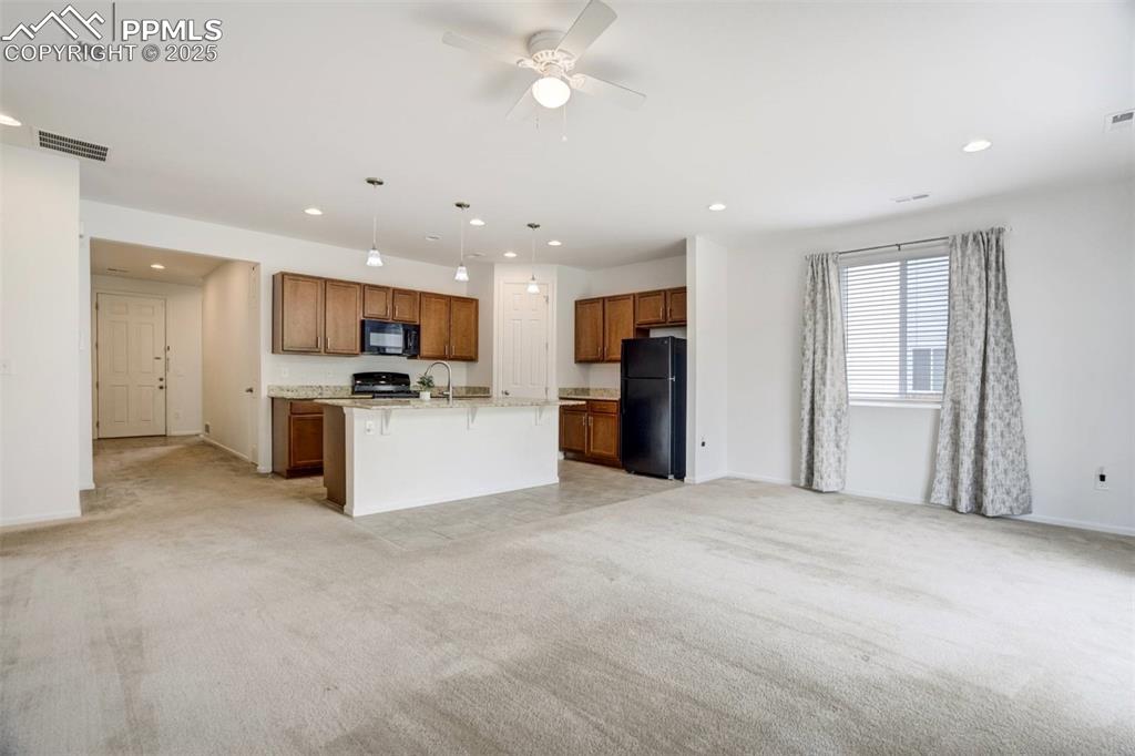 Image 6 of 36: Kitchen with black appliances, light carpet, open floor plan, brown cabinet