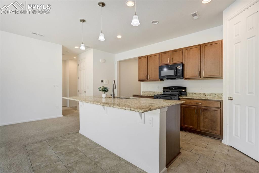 Image 9 of 36: Kitchen with black appliances, an island with sink, light stone counters, d