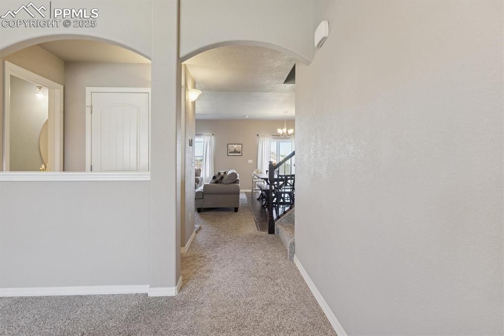 Image 10 of 45: Hall featuring arched walkways, light colored carpet, a textured ceiling, a