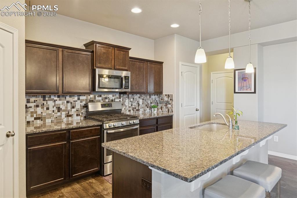 Image 22 of 45: Kitchen featuring dark brown cabinetry, appliances with stainless steel fin