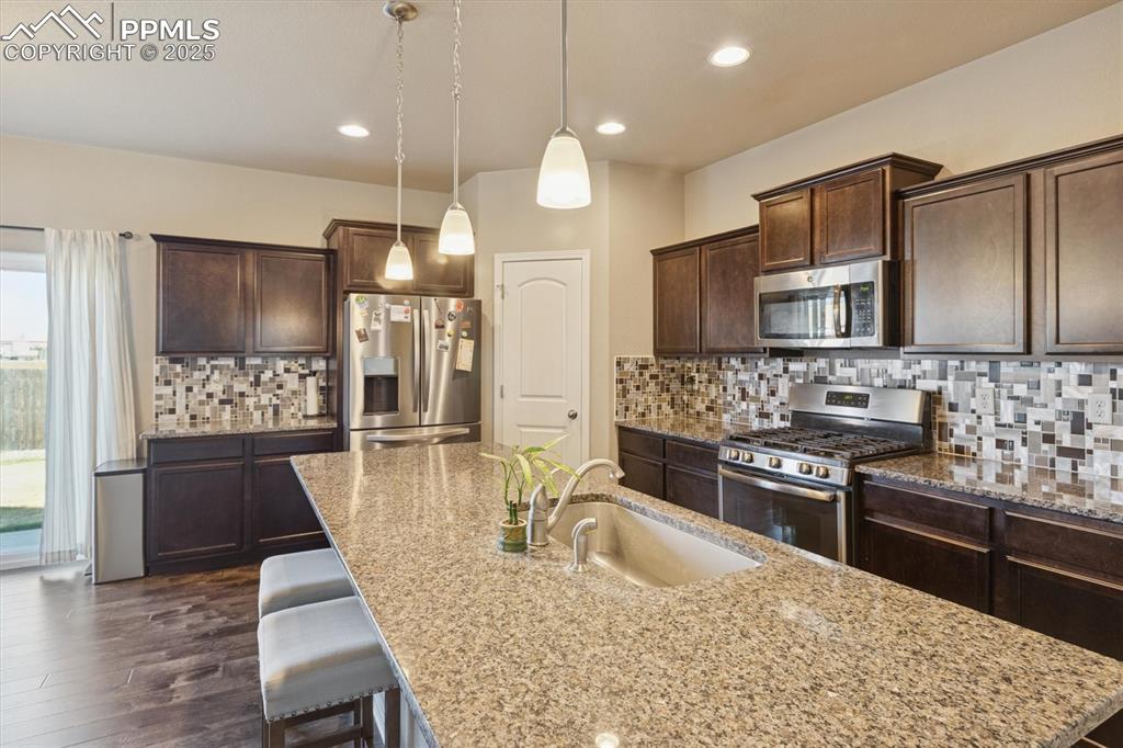 Image 25 of 45: Kitchen featuring stainless steel appliances, dark brown cabinetry, pendant