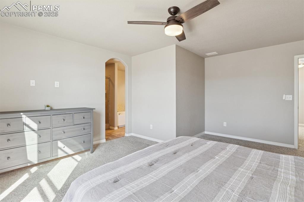 Image 30 of 45: Carpeted bedroom with arched walkways, ceiling fan, and connected bathroom