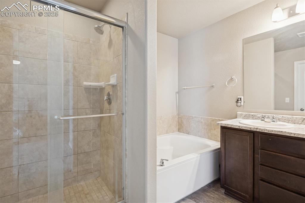 Image 31 of 45: Full bathroom featuring a bath, vanity, a textured wall, a stall shower, an