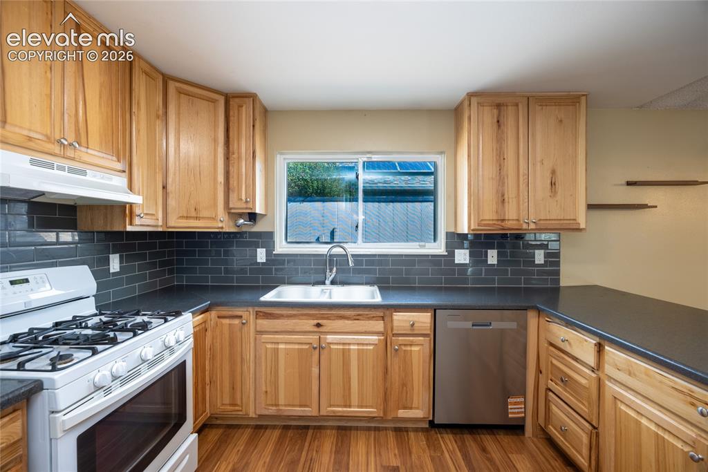 Image 12 of 26: Wood-finish flooring, natural wood cabinetry, dark subway tile backsplash, 