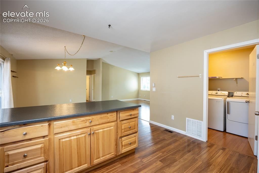 Image 13 of 26: Kitchen island with wood cabinetry and dark countertop, wood-finish floorin