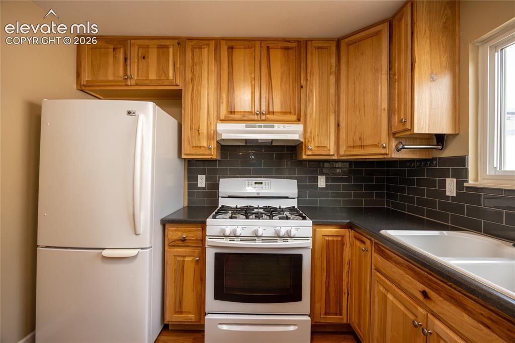 Image 14 of 26: Kitchen featuring wood cabinetry, dark countertops, subway tile backsplash,