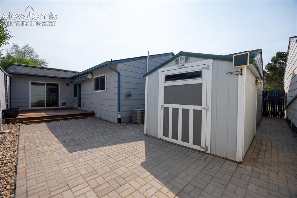 Image 25 of 26: Rear exterior with a wood deck, paver patio, and detached storage shed