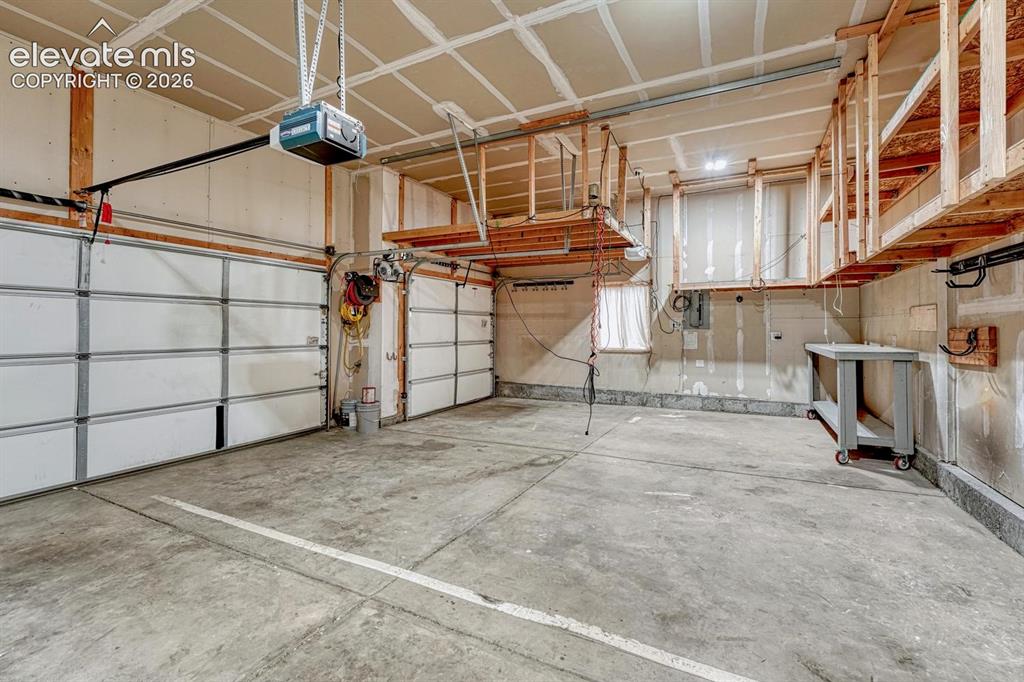 Image 43 of 50: 3-car attached garage with custom ceiling storage, work bench, and door ope