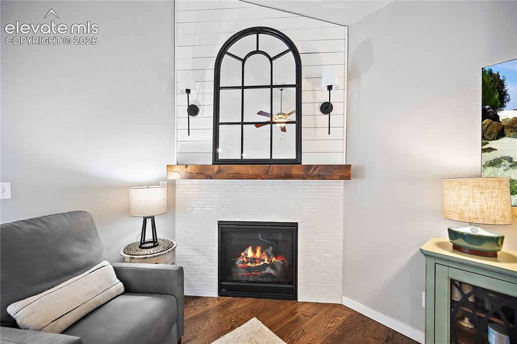 Image 7 of 44: Cozy corner gas fireplace with beautiful tile surround and wood mantel. 