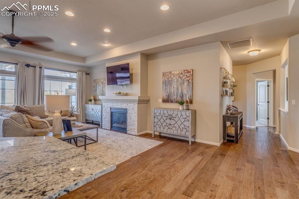 Image 18 of 50: Living room featuring a tray ceiling, wood-type flooring, a stone fireplace