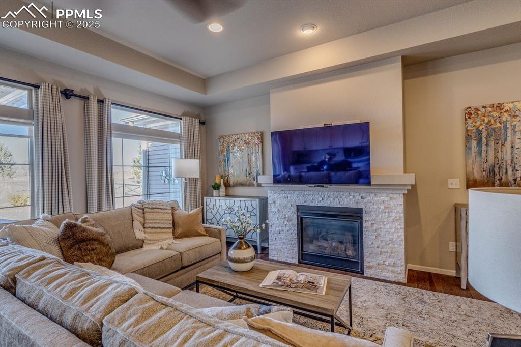 Image 20 of 50: Living area featuring a stone fireplace, a tray ceiling, wood finished floo